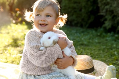 Happy little girl with cute rabbit outdoors on sunny day