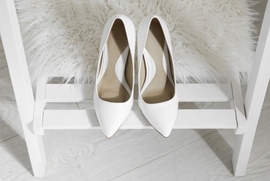 Pair of white wedding high heel shoes on wooden rack indoors, above view