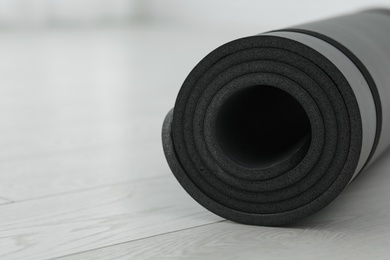 Rolled yoga mat on wooden floor, closeup. Space for text