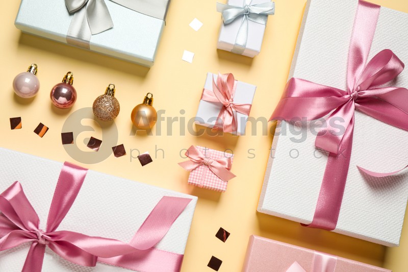 Beautiful gift boxes, Christmas balls and confetti on beige background, flat lay