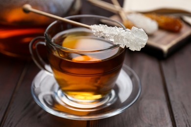 Photo of Stick with sugar crystals and cup of tea on wooden table, closeup