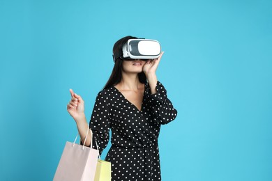 Woman with shopping bags using virtual reality headset on light blue background