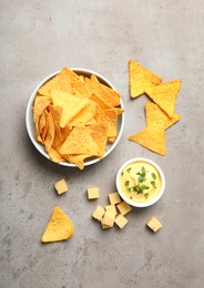 Bowl of delicious mexican nachos chips and cheese sauce on grey table, flat lay