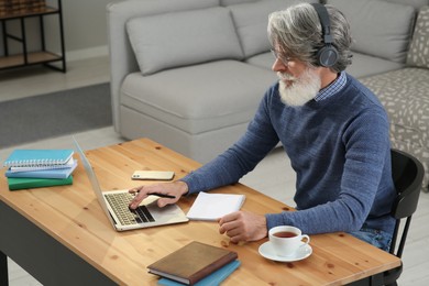 Middle aged man with laptop and headphones learning at table indoors
