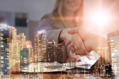 Double exposure of night cityscape and business people shaking hands in office, closeup. Team work 