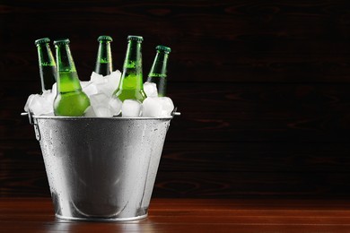 Photo of Metal bucket with bottles of beer and ice cubes on wooden background, space for text