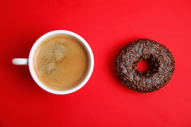 Delicious coffee and donut on red background, flat lay. Sweet pastries