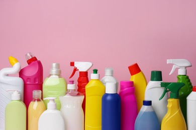 Many bottles of different detergents on pink background. Cleaning supplies