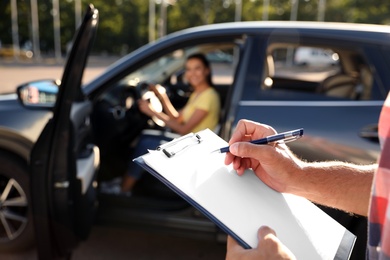 Photo of Instructor with clipboard near car outdoors, closeup. Driving school exam