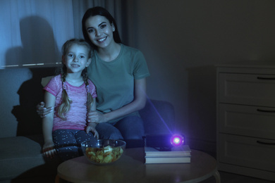 Young woman and her daughter watching movie using video projector at home