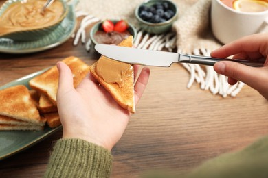 Photo of Woman spreading peanut butter onto toast at wooden table, closeup