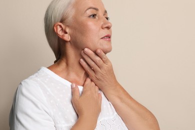Mature woman doing thyroid self examination on beige background