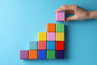 Photo of Woman holding wooden cube near others on light blue background, top view. Management concept
