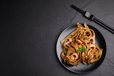 Photo of Tasty buckwheat noodles with shrimps on black table, flat lay. Space for text