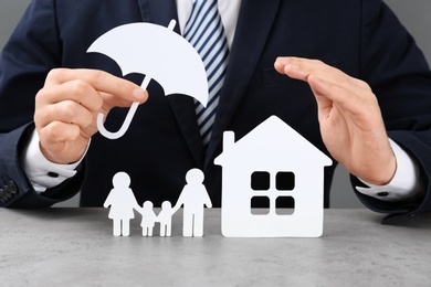 Man with cutout paper family, house and umbrella at table, closeup. Life insurance concept