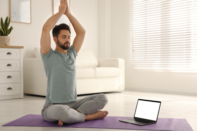 Man practicing yoga while watching online class at home during coronavirus pandemic. Social distancing