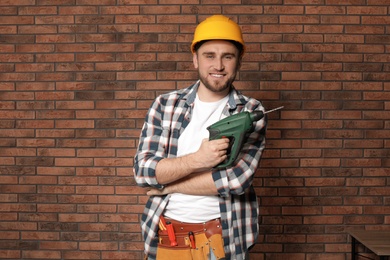 Young working man with modern electric drill near brick wall