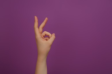 Woman showing two fingers on purple background, closeup. Space for text