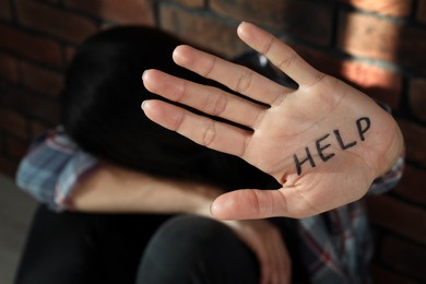 Domestic violence concept. Unhappy woman near brick wall, focus on hand with written word Help
