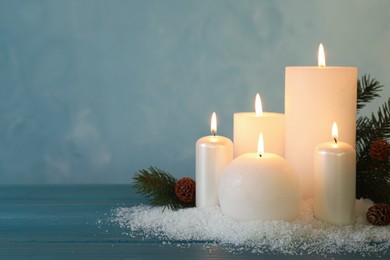 Burning candles with fir tree branch, cones and artificial snow on blue wooden table, space for text. Christmas atmosphere