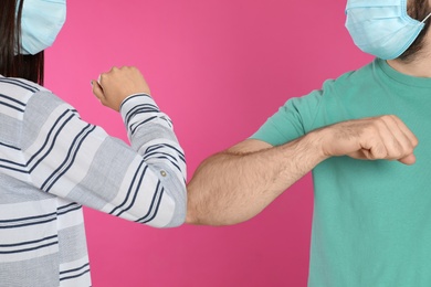 Man and woman bumping elbows to say hello on pink background, closeup. Keeping social distance during coronavirus pandemic