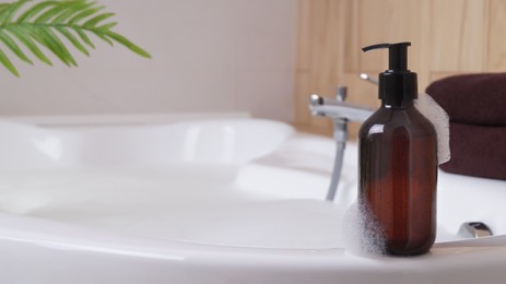 Bottle of bubble bath with foam on tub indoors, space for text