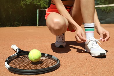 Woman tying shoelaces and tennis racket with ball on court, closeup