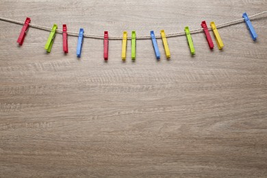 Colorful plastic clothespins and rope on wooden background. Space for text