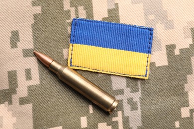 Photo of Military patch and bullet on pixel Ukrainian camouflage, flat lay