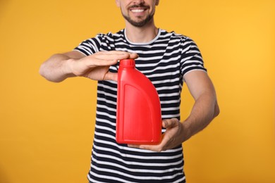 Man showing red container of motor oil on orange background, closeup