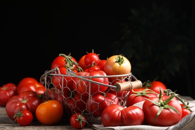 Many different ripe tomatoes on wooden table against dark background