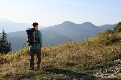 Tourist with backpack in mountains on sunny day, back view. Space for text