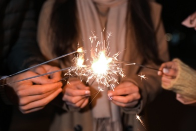 Group of people in warm clothes holding burning sparklers, closeup