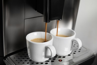 Espresso machine pouring coffee into cups against light background, closeup