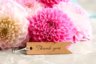 Paper tag with phrase Thank You and bouquet of dahlias on marble table, closeup