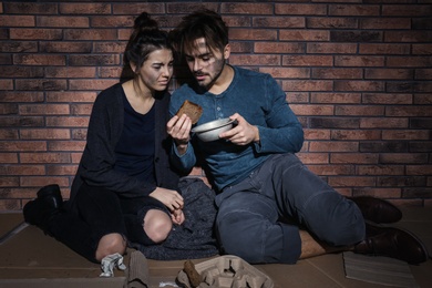 Poor young couple with bread on floor near brick wall
