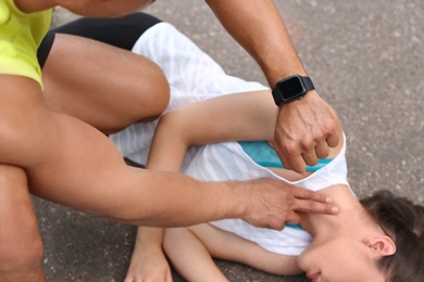 Young man checking pulse of unconscious woman on street, closeup