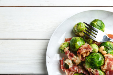 Delicious Brussels sprouts with bacon on white wooden table, top view. Space for text