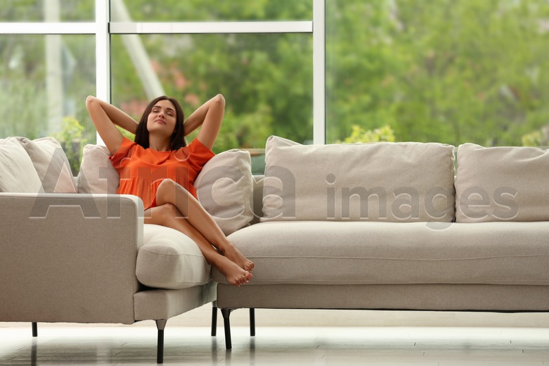 Young woman relaxing on sofa at home, space for text