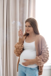 Young pregnant woman smoking cigarette at home. Harm to unborn baby