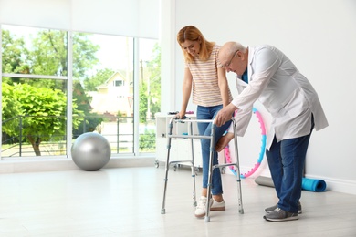 Doctor helping woman with walking frame indoors