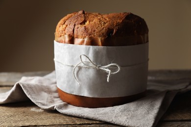 Photo of Delicious Panettone cake wrapped in parchment paper on wooden table. Traditional Italian pastry