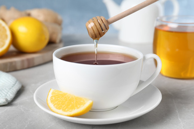 Photo of Honey pouring into cup with tea from wooden dipper on light grey marble table, closeup