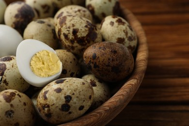 Photo of Unpeeled and peeled hard boiled quail eggs in bowl on wooden table, closeup