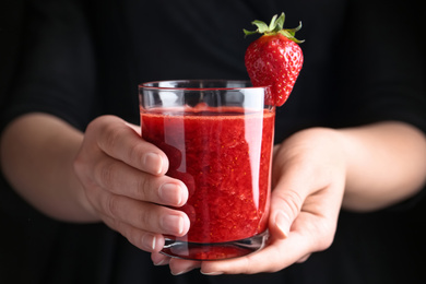 Woman holding tasty strawberry smoothie on black background, closeup
