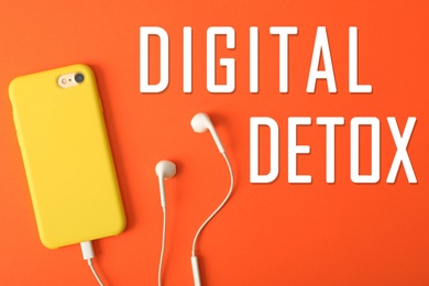 Text Digital Detox, modern phone with earphones on bright orange background, top view