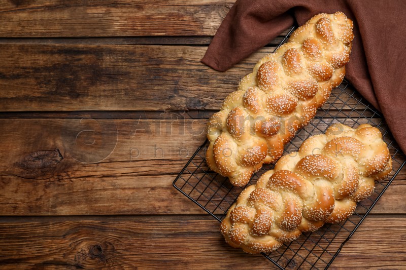 Photo of Homemade braided breads and cooling rack on wooden table, top view with space for text. Traditional Shabbat challah