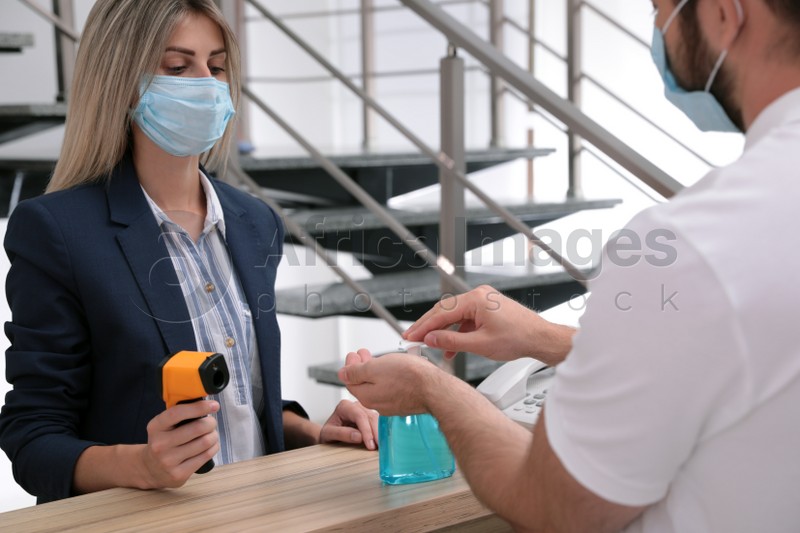 Photo of Man applying hand sanitizer at office reception