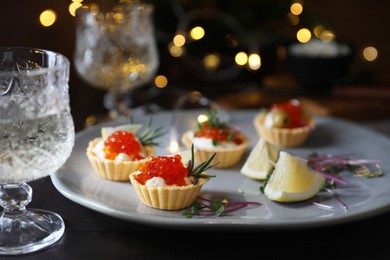 Photo of Delicious tartlets with red caviar served on black table against blurred festive lights, closeup. Space for text