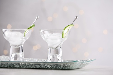 Glasses of martini with cucumber on table against light background. Space for text